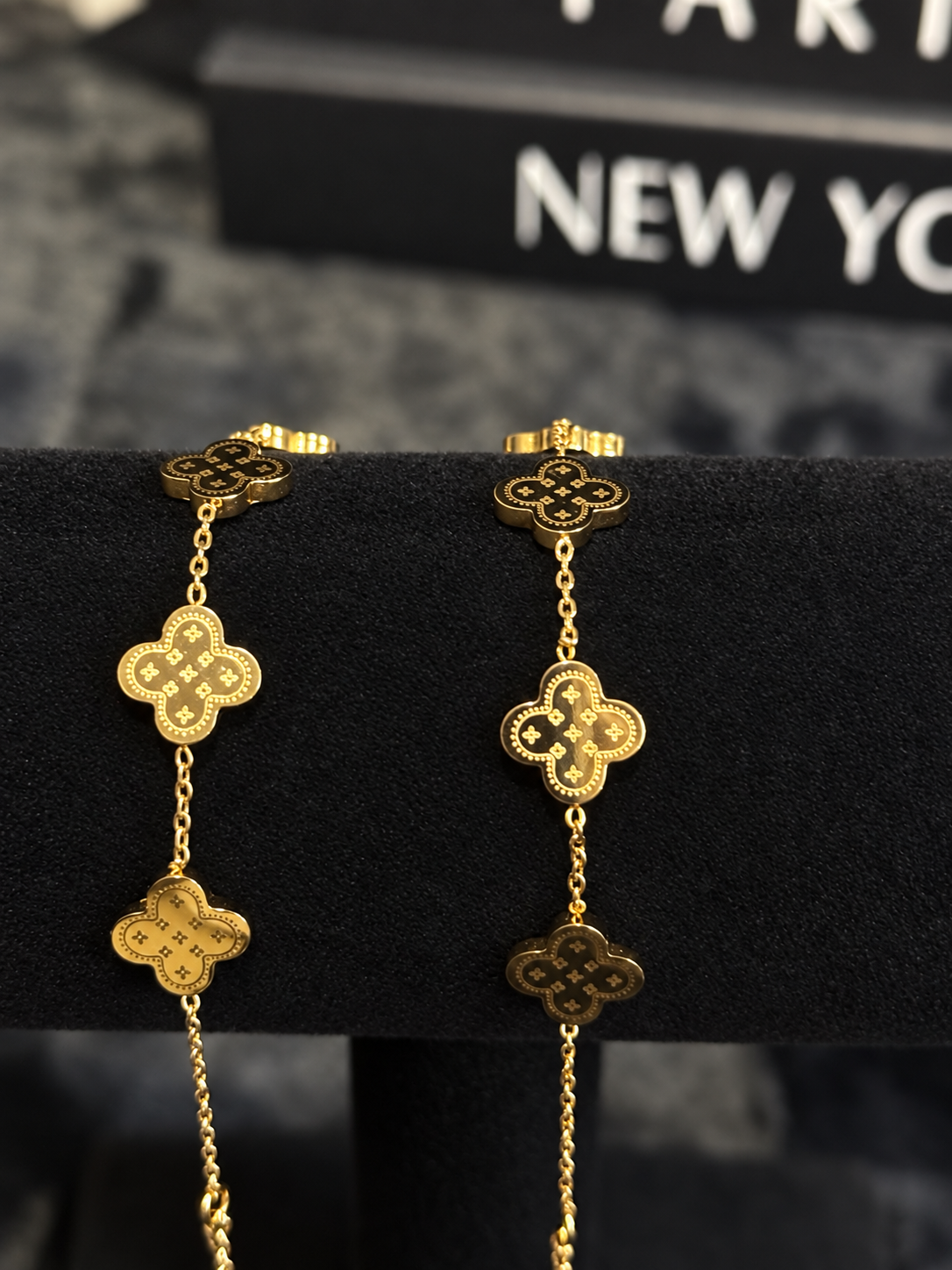 Gold-toned bracelets with detailed clover-shaped motifs on a black velvet display