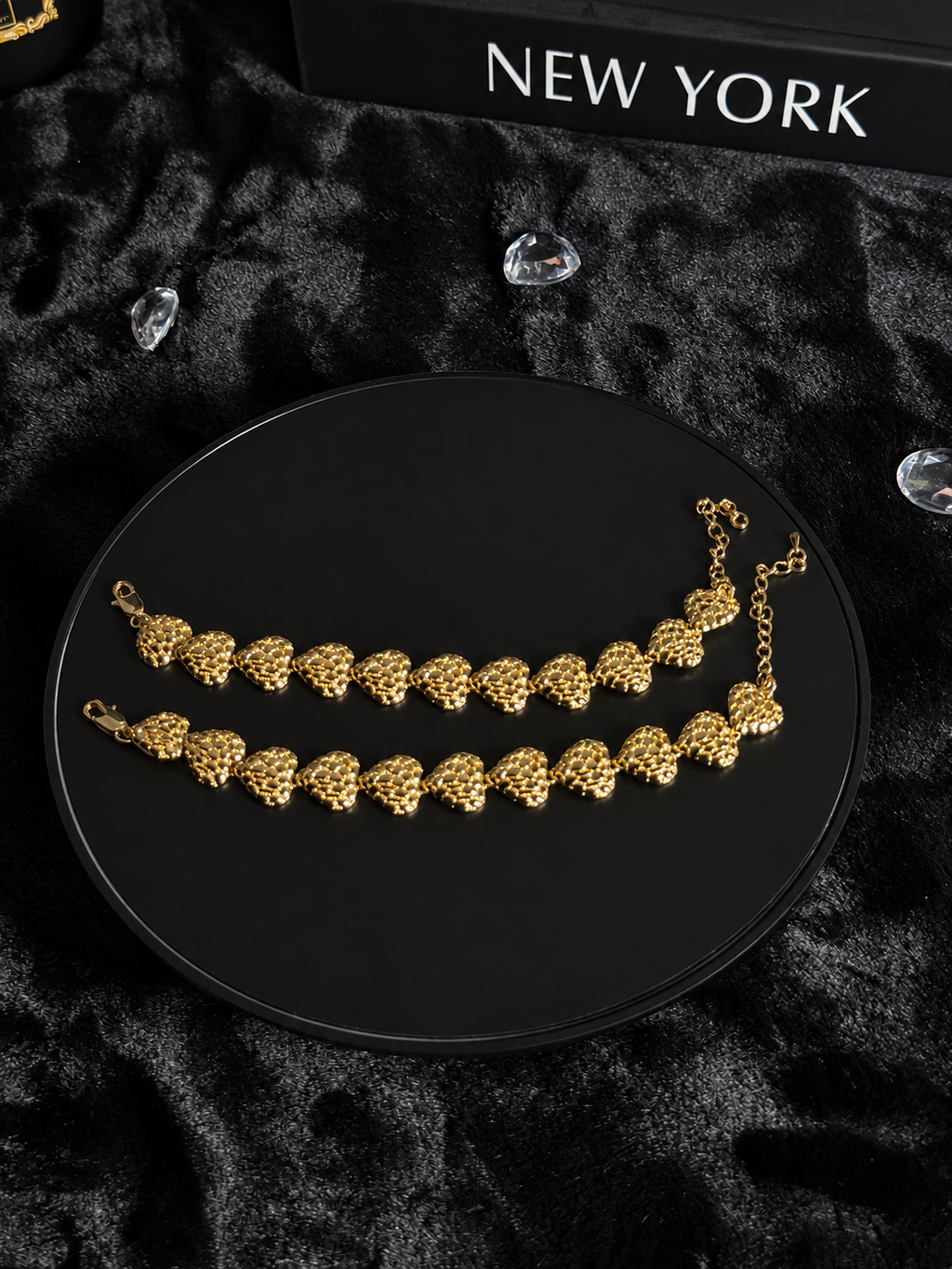 Gold-toned bracelets with textured heart-shaped links on a black display